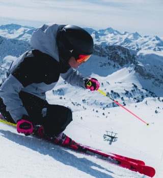 Skier carving a fast turn at Baqueira Beret under blue skies, with the ski area and Pyrenean peaks beyond