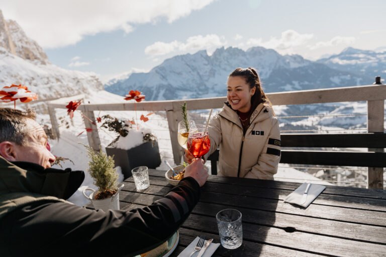 Two skiers raising an aperitivo on a sunny mountain terrace in Carezza Dolomites