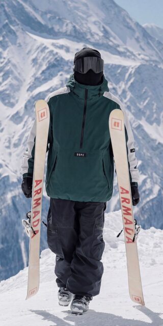 Skier carrying Armada skis wearing a green Dope Snow anorak