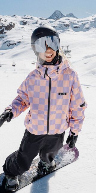Smiling snowboarder in a checked Dope Snow jacket on the piste