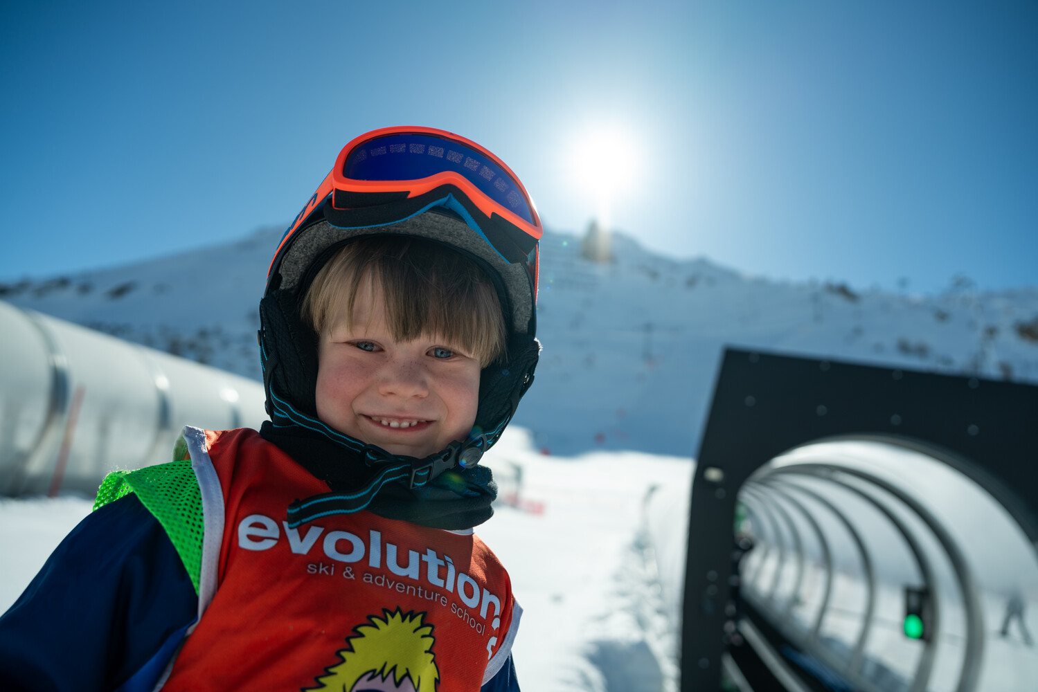 Smiling young skier in an Evolution 2 Kids Club bib beside the magic carpet in Tignes