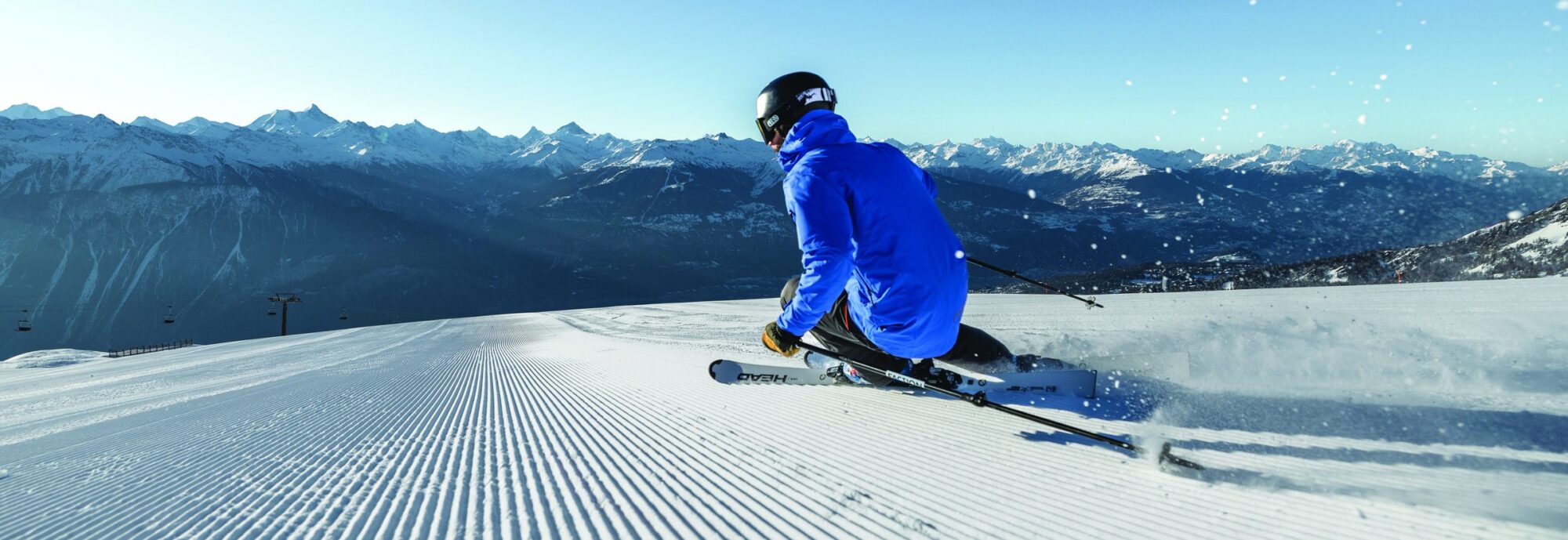 Skier carving fresh corduroy on an empty early-season piste above the Rhône Valley in Crans-Montana