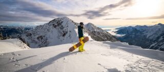 Snowboarder on a ridge at Kicking Horse Mountain Resort above a cloud-filled valley, Golden BC