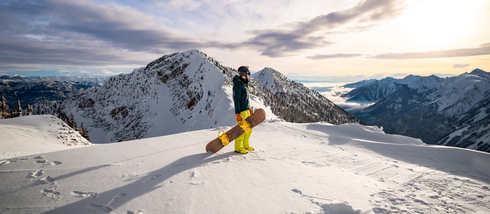 Snowboarder on a ridge at Kicking Horse Mountain Resort above a cloud-filled valley, Golden BC