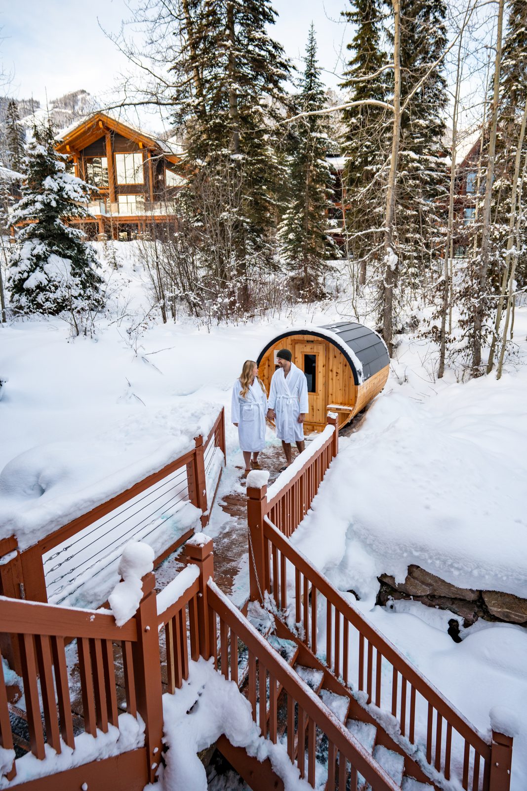 Couple in robes beside an outdoor barrel sauna in the snow near Golden BC
