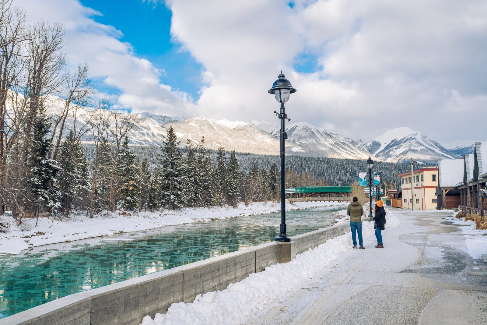 Couple walking beside the Kicking Horse River in Golden, British Columbia, with snowy mountains behind