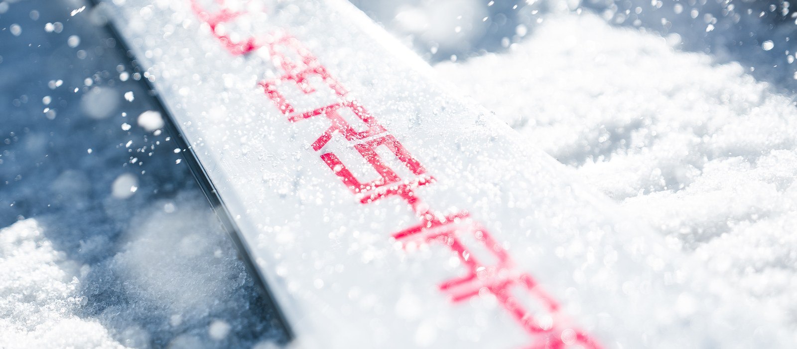 Close-up of the SUPERSHAPE lettering on a white HEAD ski topsheet covered in fresh snow