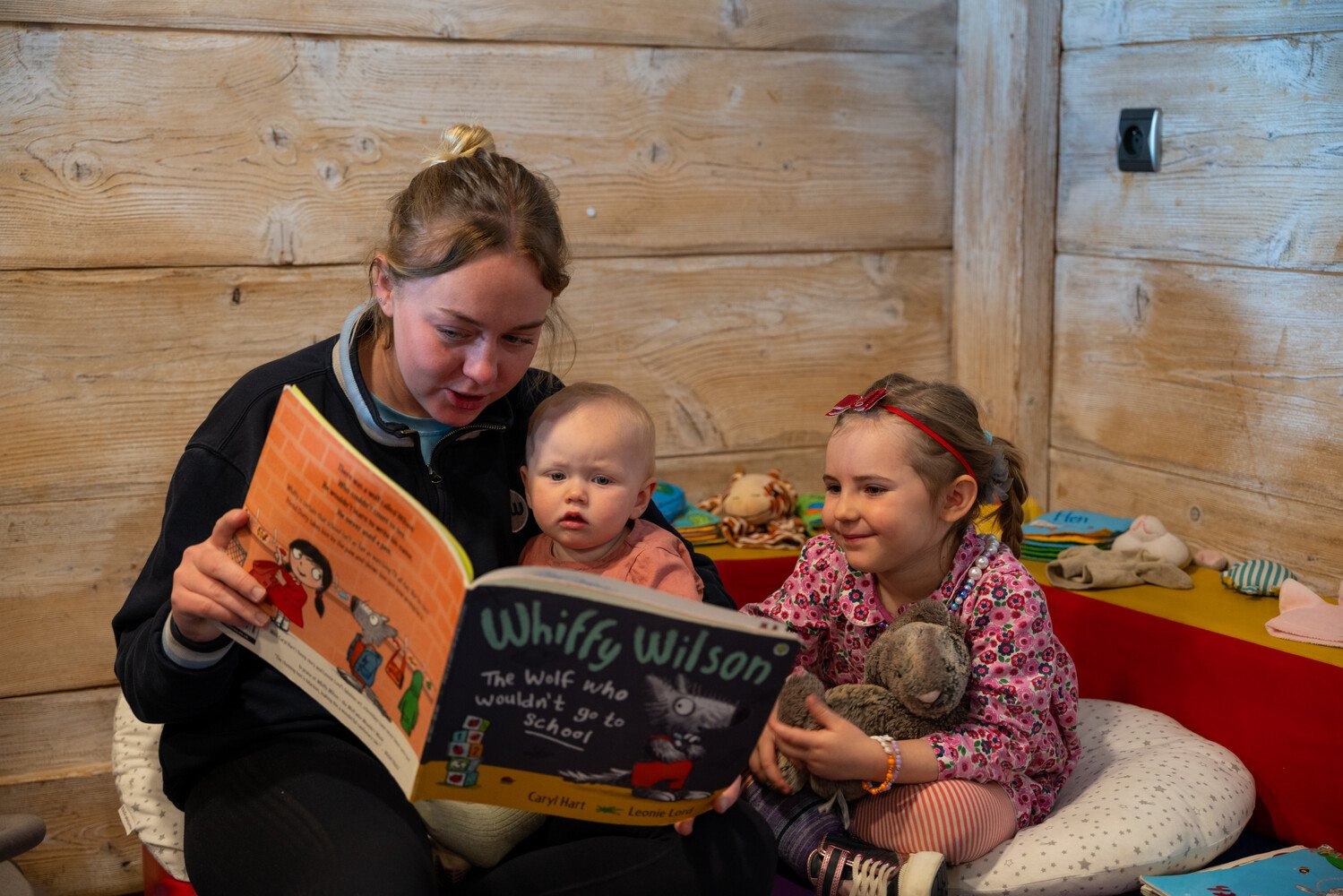 Mark Warner childcare nanny reading a story to a baby and young girl in Tignes