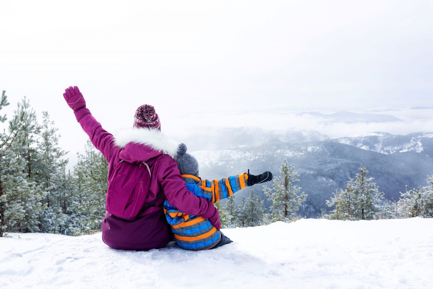 Parent and child sitting in the snow looking out over the mountains on a family ski holiday