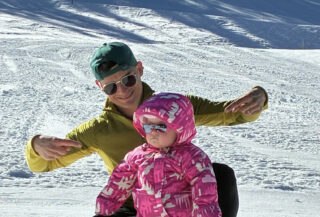Grandfather skiing with his toddler granddaughter in La Clusaz during a three-generation family ski holiday