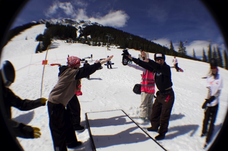 Quay Queens riders cheering with hands raised beside a rail feature in the Norquay terrain park