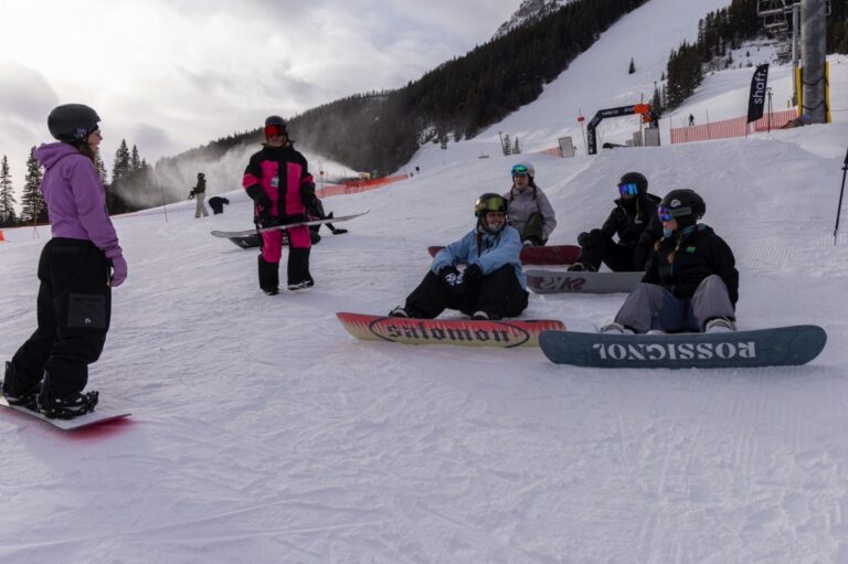 Quay Queens members relaxing on their snowboards at the base of the Norquay terrain park, Banff