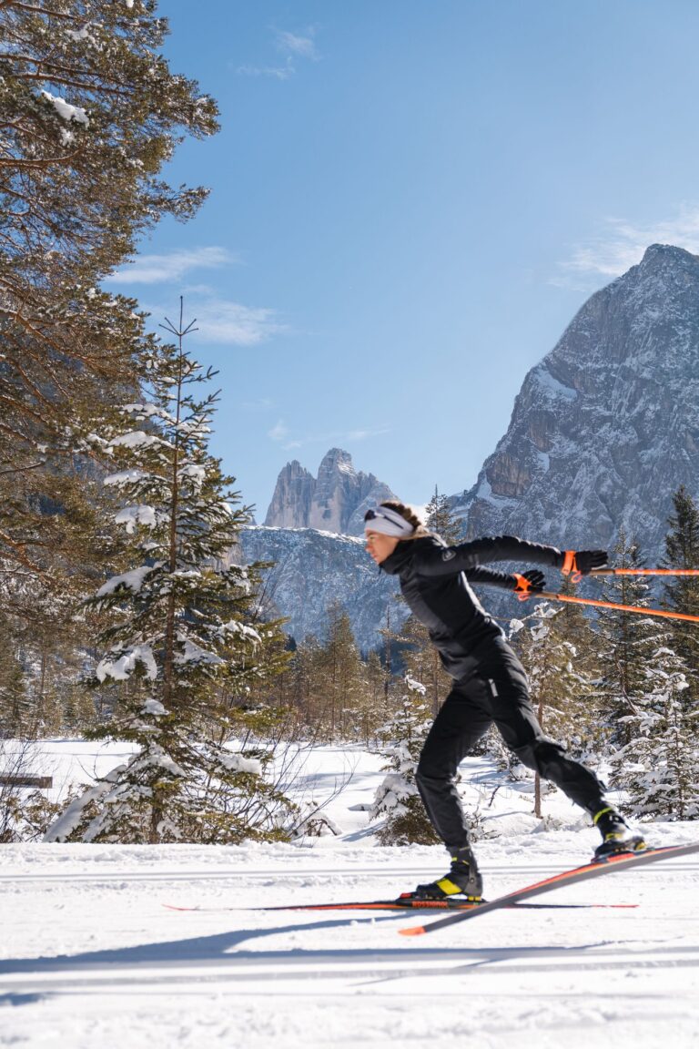 Cross-country skier gliding through snowy pines with the Three Peaks rising behind in the 3 Zinnen Dolomites