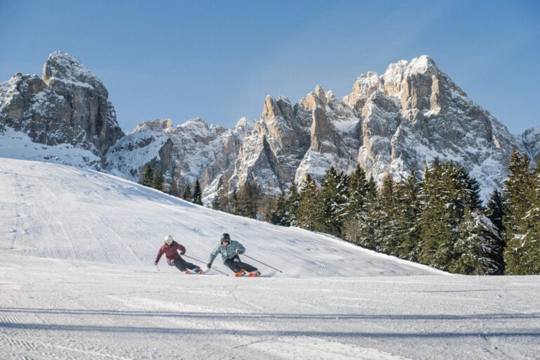 Two skiers carving below jagged rock towers in the 3 Zinnen Dolomites