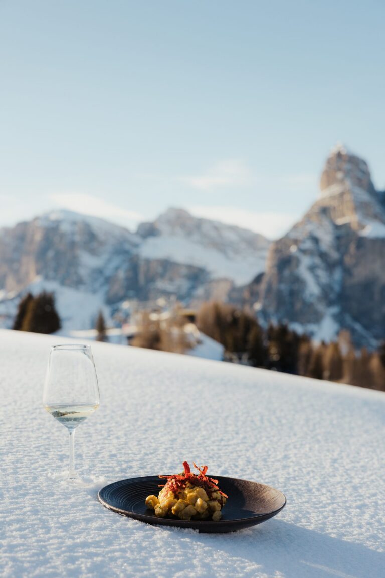 Chef-created gnocchi dish and a glass of white wine set in the snow in Alta Badia