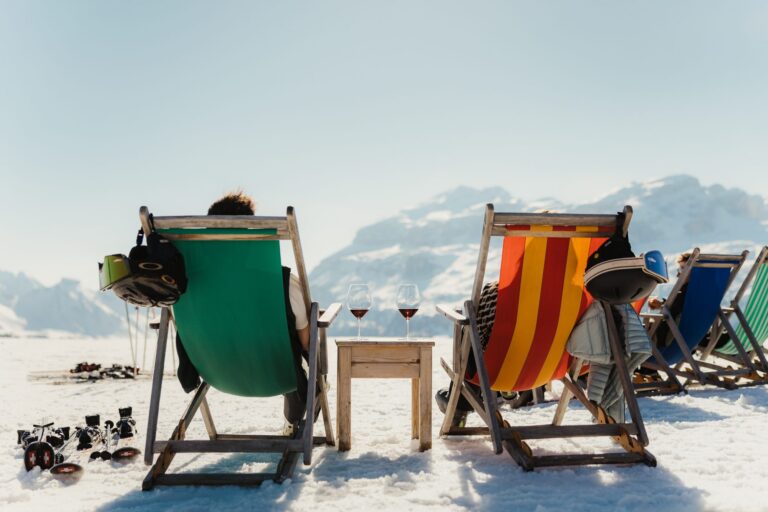 Two skiers relaxing in colourful deckchairs with glasses of red wine in Alta Badia