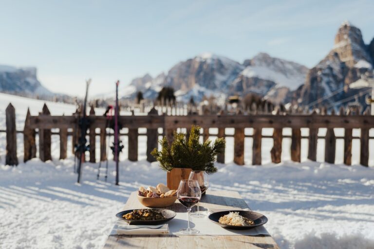 Pasta, red wine and bread on a sunny mountain hut table in Alta Badia with the Sassongher behind