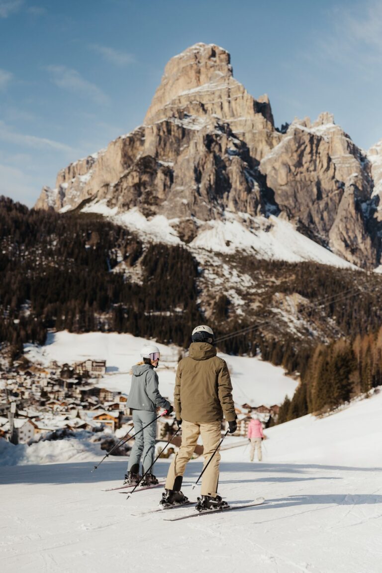 Two skiers looking down on Corvara village beneath the Sassongher peak in Alta Badia