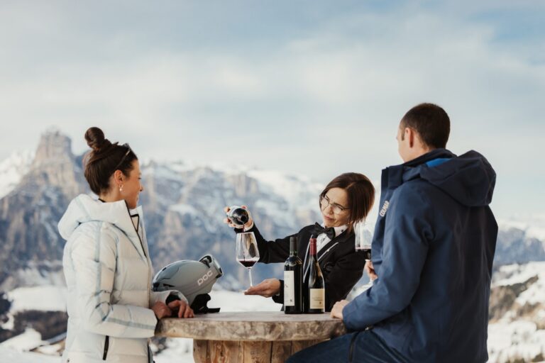 Sommelier pouring South Tyrolean red wine for two skiers on the slopes in Alta Badia
