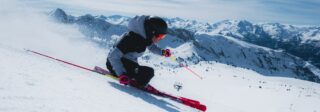 Skier carving a fast turn at Baqueira Beret under blue skies, with the ski area and Pyrenean peaks beyond