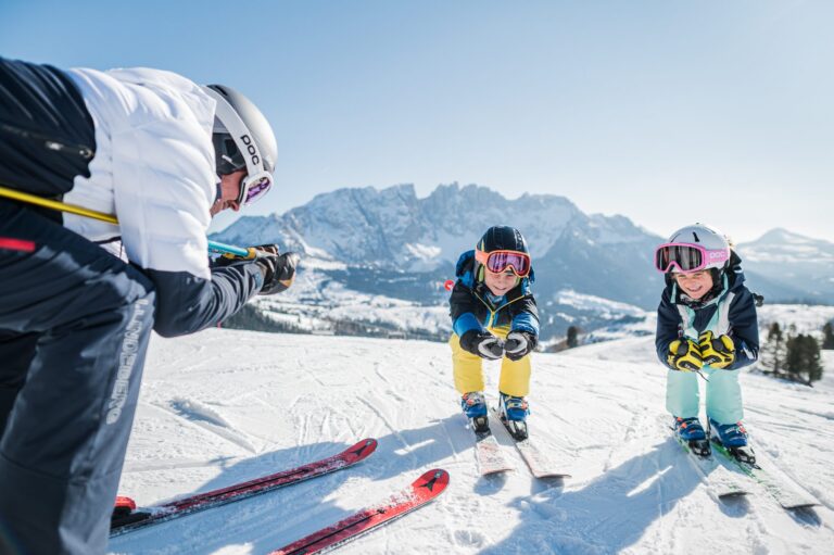 Two young children skiing towards their instructor on a sunny slope in Carezza Dolomites