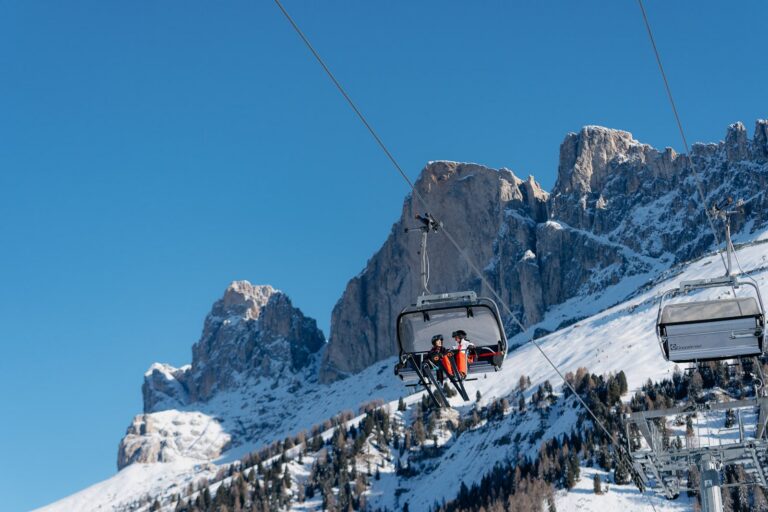 Two skiers carving in Carezza Dolomites as the Rosengarten glows pink at sunset