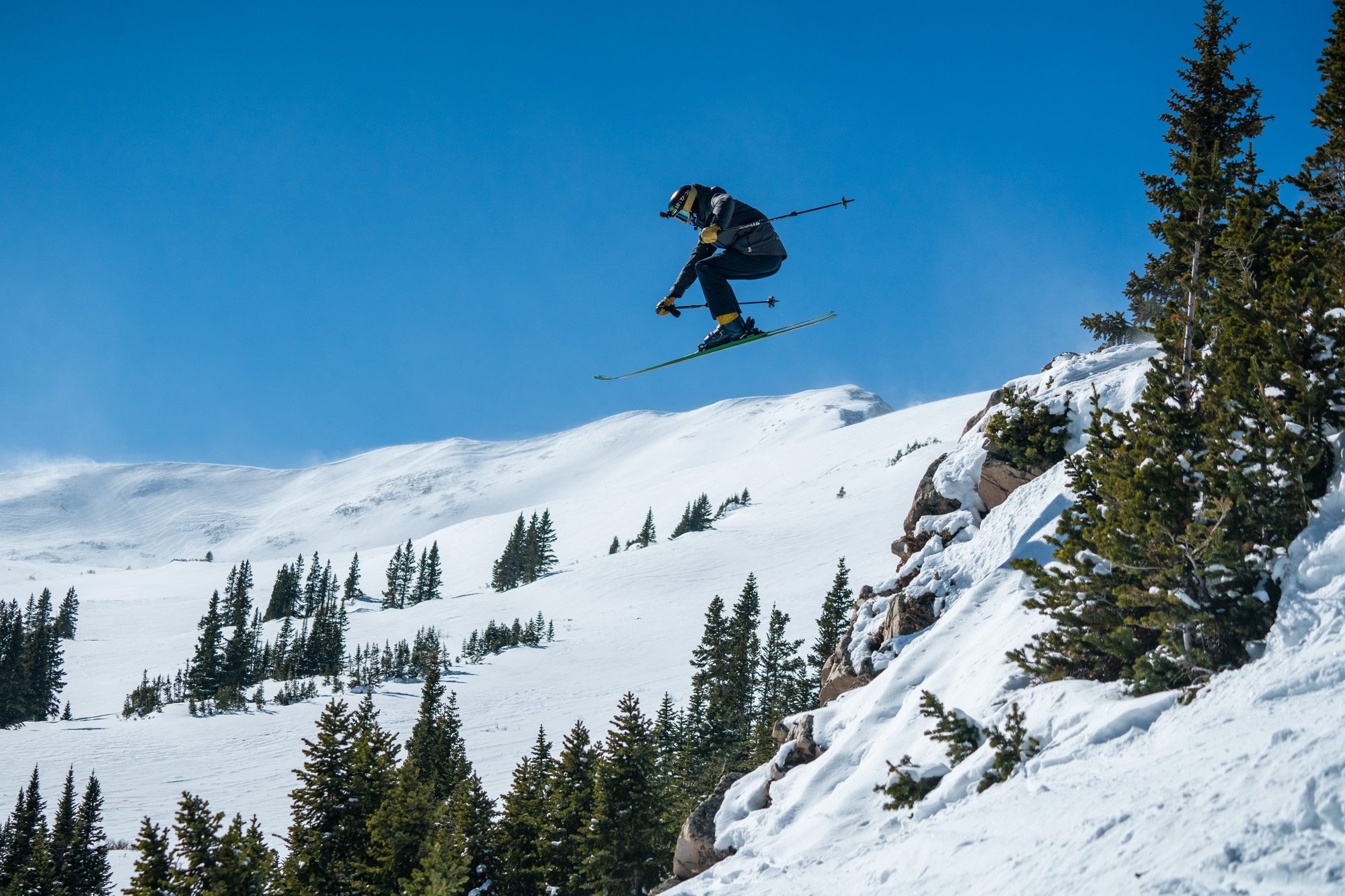 Skier jumping off a rocky ledge among the trees at Copper Mountain