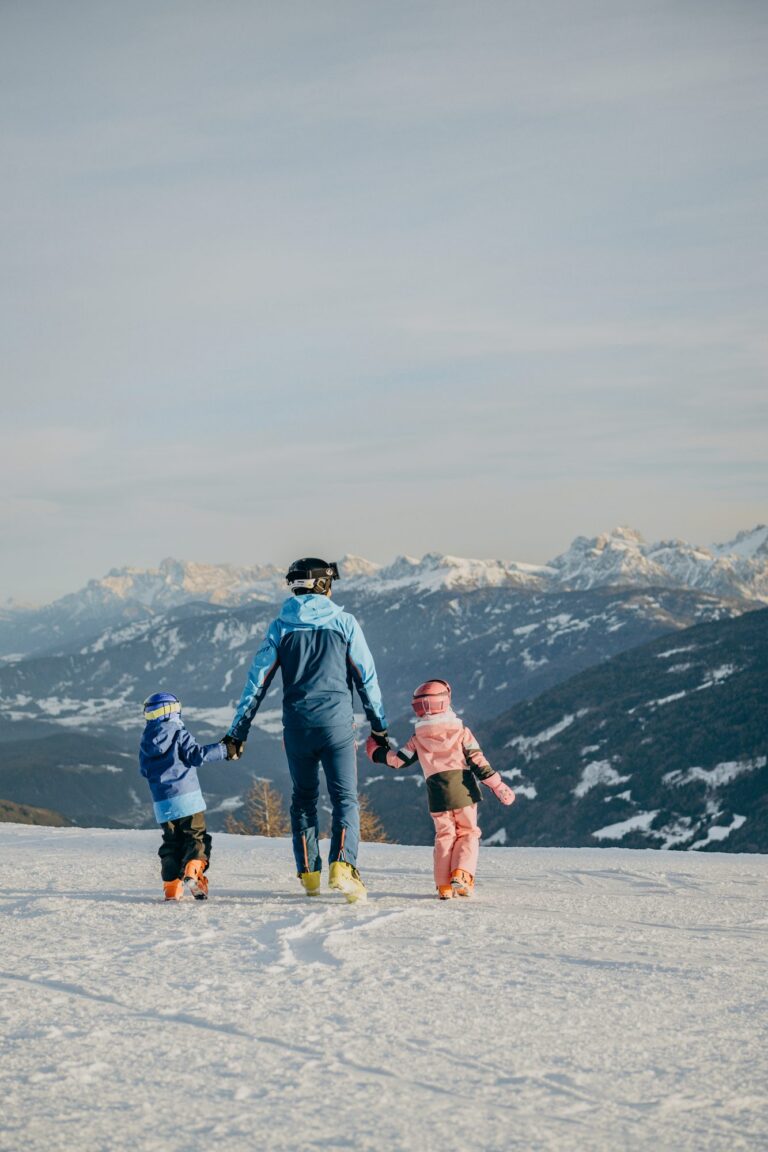 Parent holding hands with two children on a piste in Gitschberg Jochtal looking towards the Dolomites