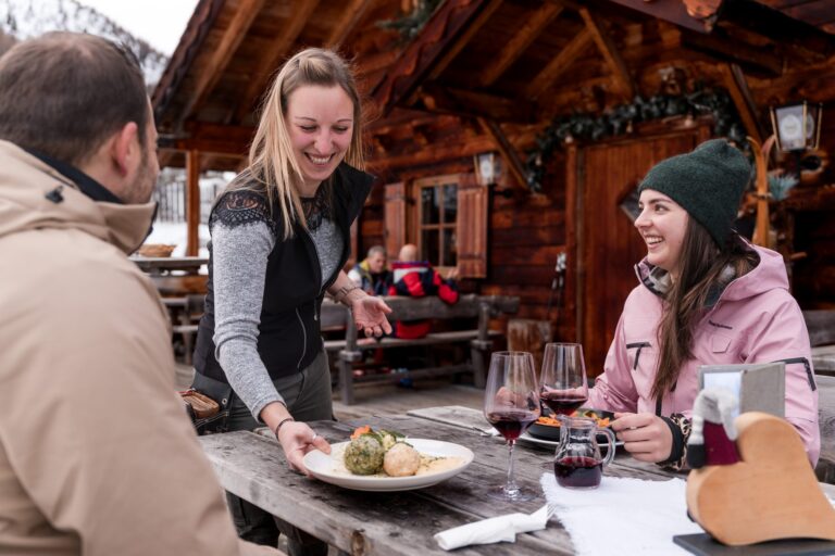 Waitress serving South Tyrolean dumplings to skiers on a mountain hut terrace in Gitschberg Jochtal