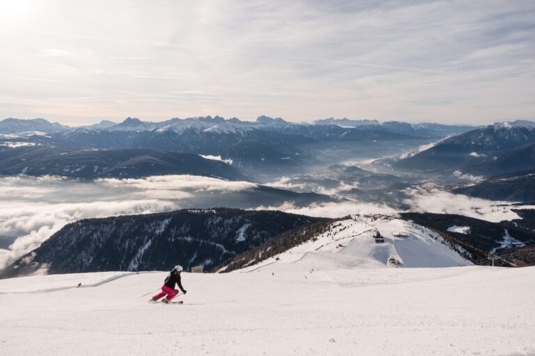 Skier carving down a wide piste in Gitschberg Jochtal above a sea of cloud with the Dolomites beyond
