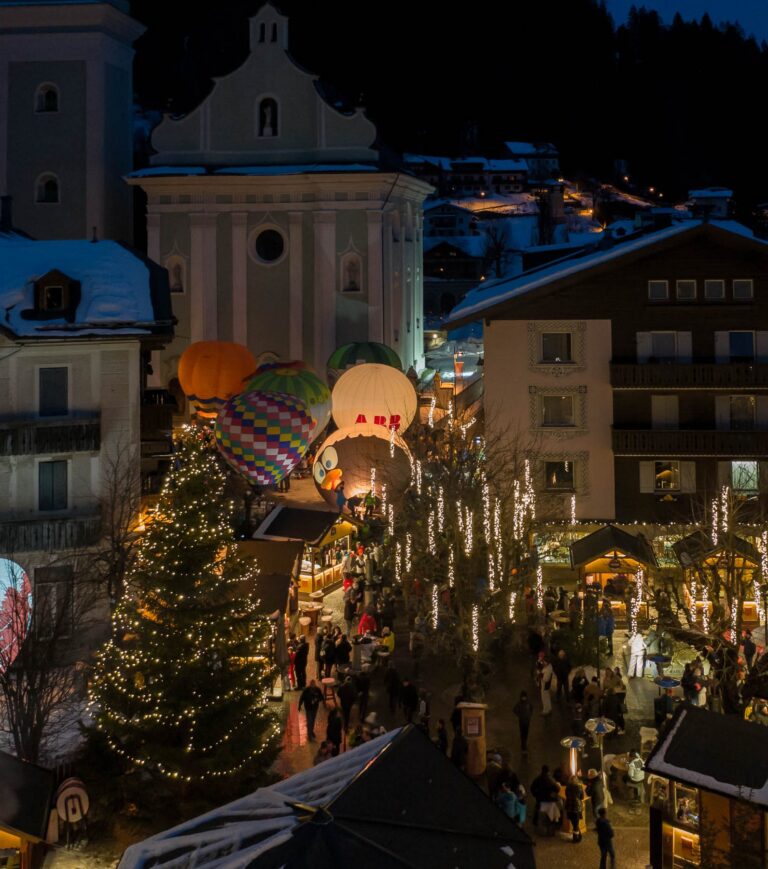 Innichen Christmas market lit up at dusk with hot air balloons in front of the church