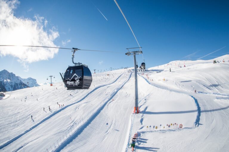 Gondola above busy pistes and a fun slope on Kronplatz on a sunny day