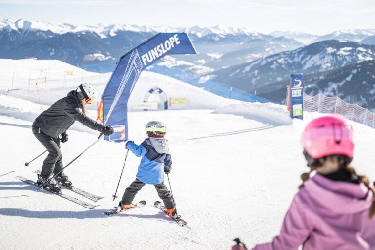 Parent helping a young child through the Funslope on Kronplatz with a sister watching