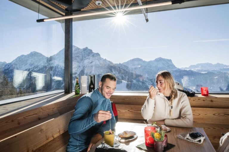 Couple enjoying tea and pastries by a panoramic window in a mountain hut on Kronplatz