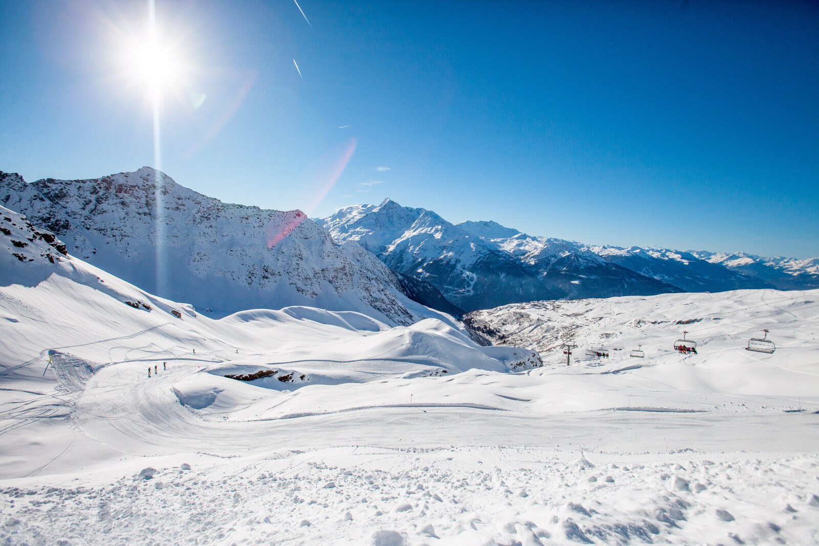 Sunny, uncrowded pistes and chairlift at La Rosière with snowy peaks of the Tarentaise Valley behind