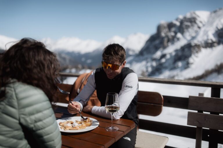 Couple enjoying Kaiserschmarrn and white wine on a sunny mountain hut terrace in Ladurns