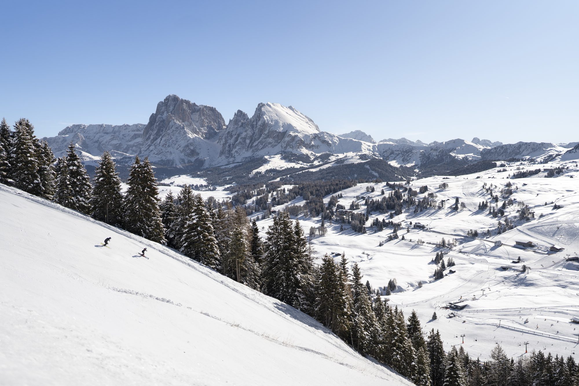 Two skiers on a slope above the snowy Seiser Alm plateau with the Langkofel and Plattkofel in the distance
