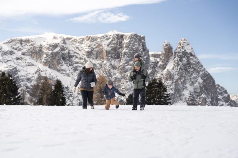 Family on a winter walk in fresh snow on the Seiser Alm with the Schlern behind
