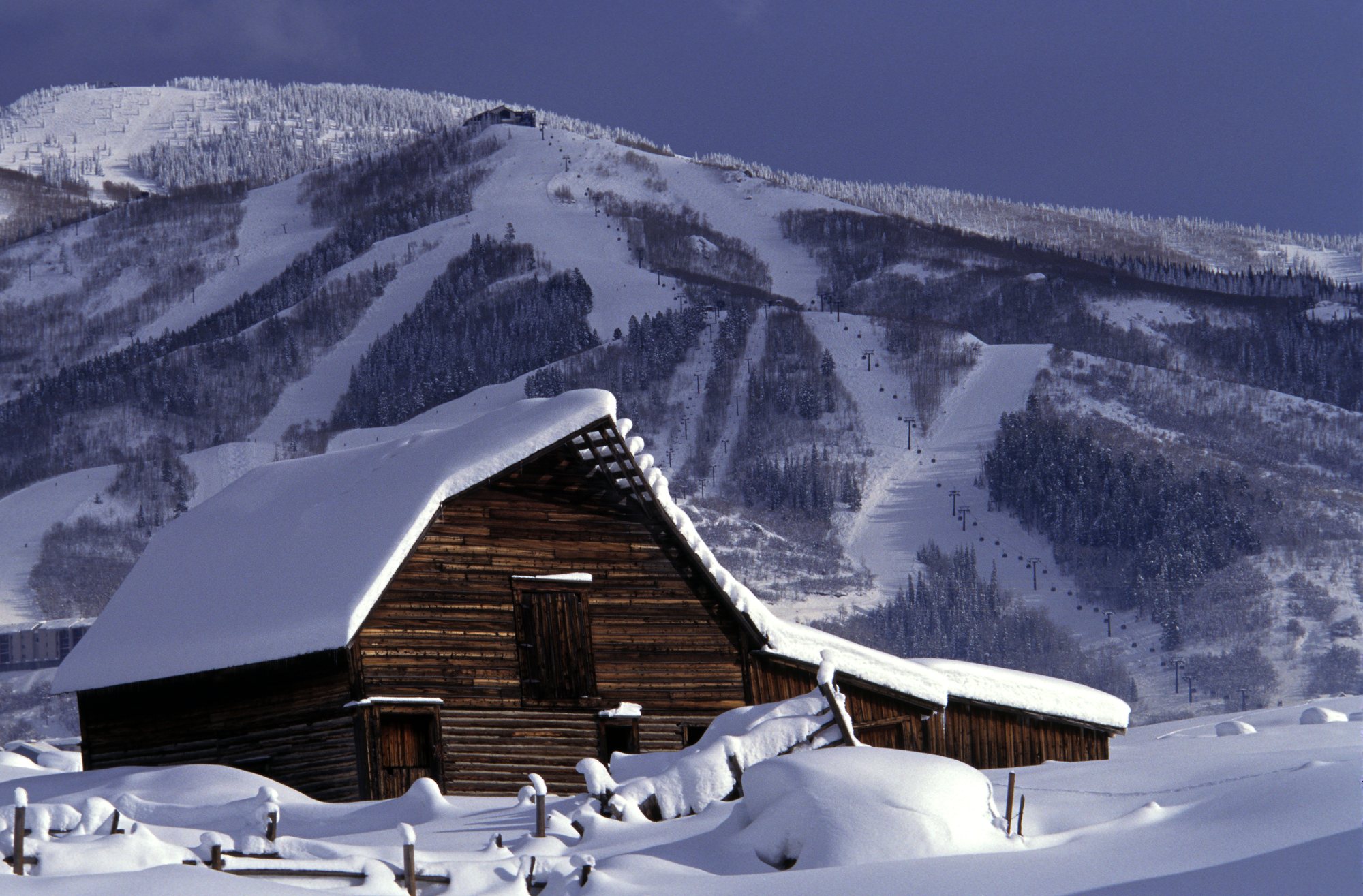 Historic wooden barn under deep snow with the Steamboat ski area behind
