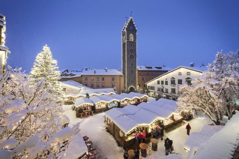 Sterzing Christmas market at dusk with wooden stalls and the Zwölferturm tower