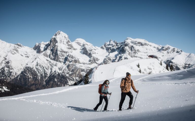 Two snowshoers walking through deep snow with jagged peaks behind in Sterzing-Ratschings-Gossensass