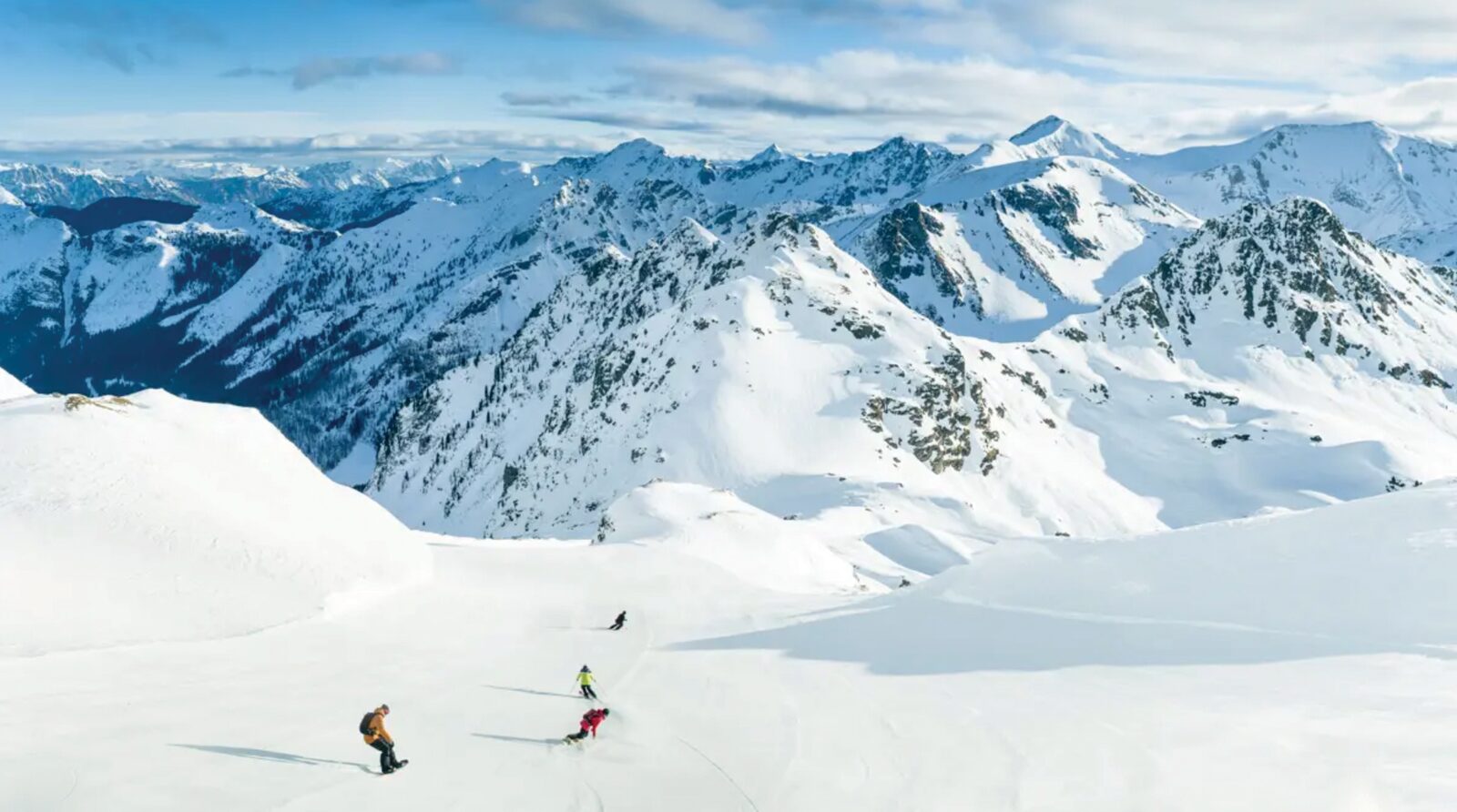 Skiers and snowboarders on a wide, empty slope with snowy peaks behind